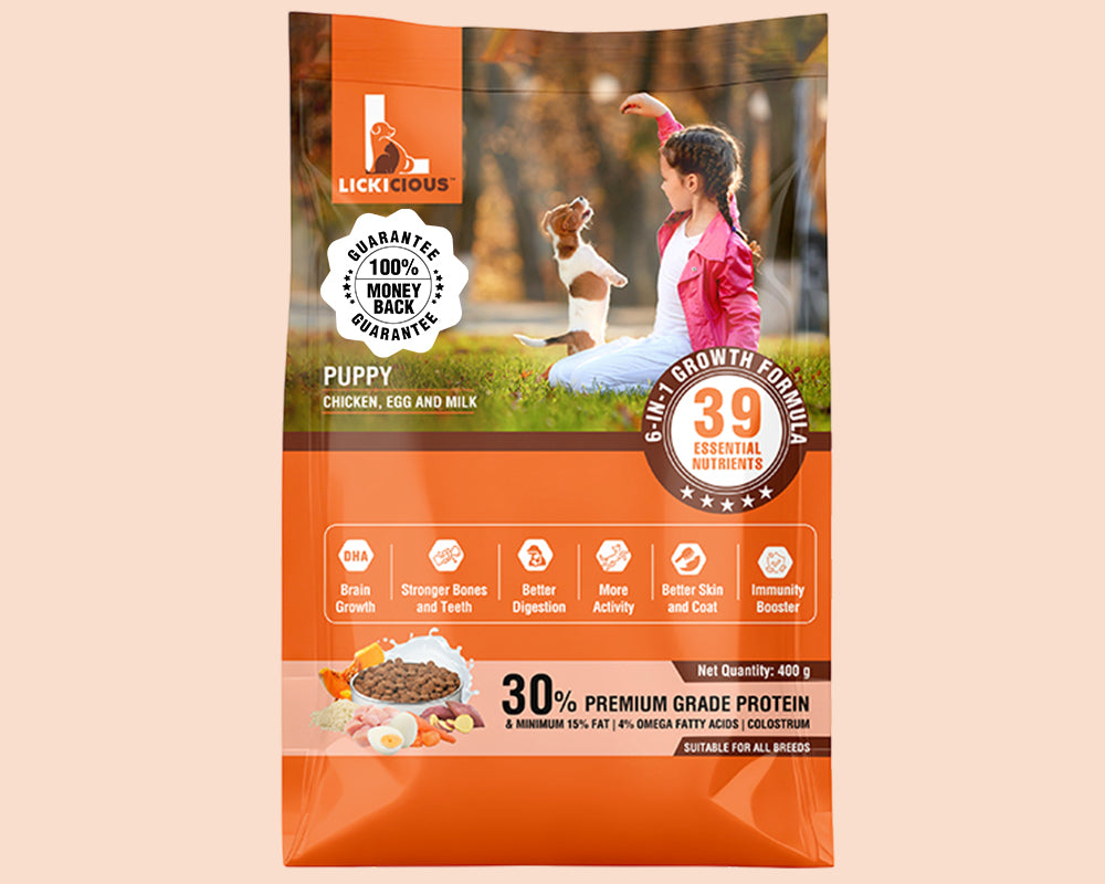 A bag of Lickicious Puppy Chicken, Egg and Milk formula dog food, featuring a bright orange design with a photo of a woman and her dog on a grassy field, and product details for a 400g pack.